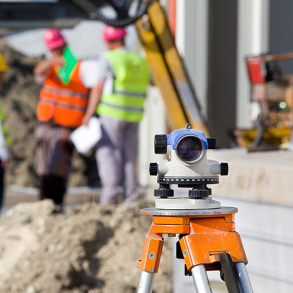 Surveying measuring equipment level theodolite on tripod at construction site with workers in background