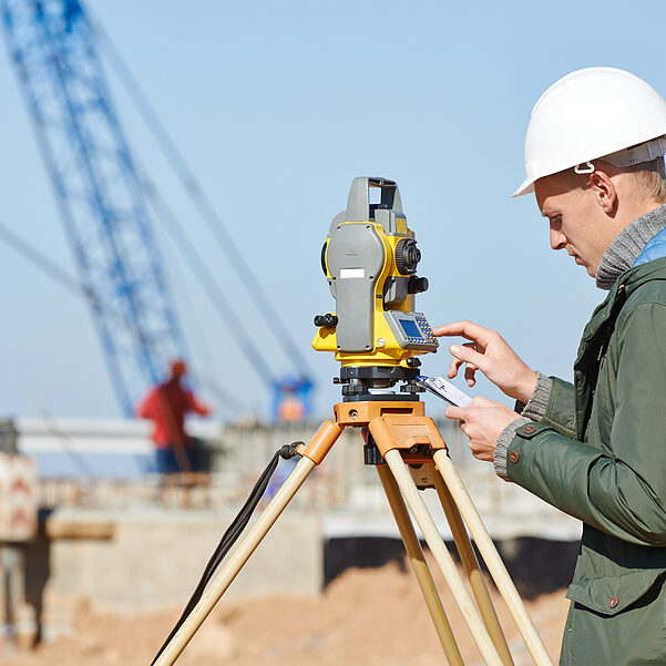 Surveyor builder worker with theodolite transit equipment at construction site outdoors during surveying work